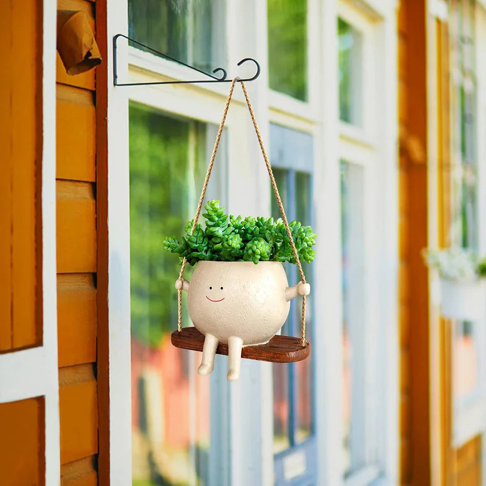 Smiling face planter with succulents hanging outside a window on a black hook