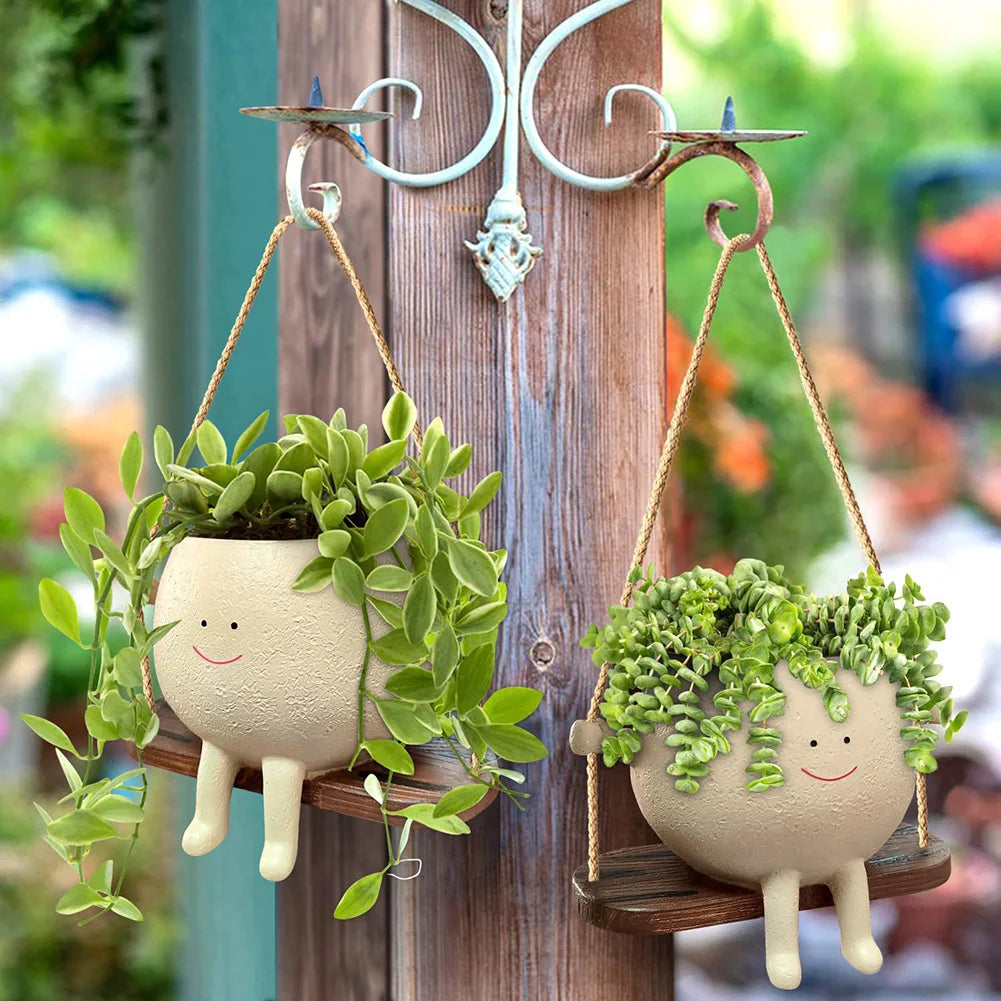 Two smiling face planters with trailing plants hanging from hooks on a wooden post