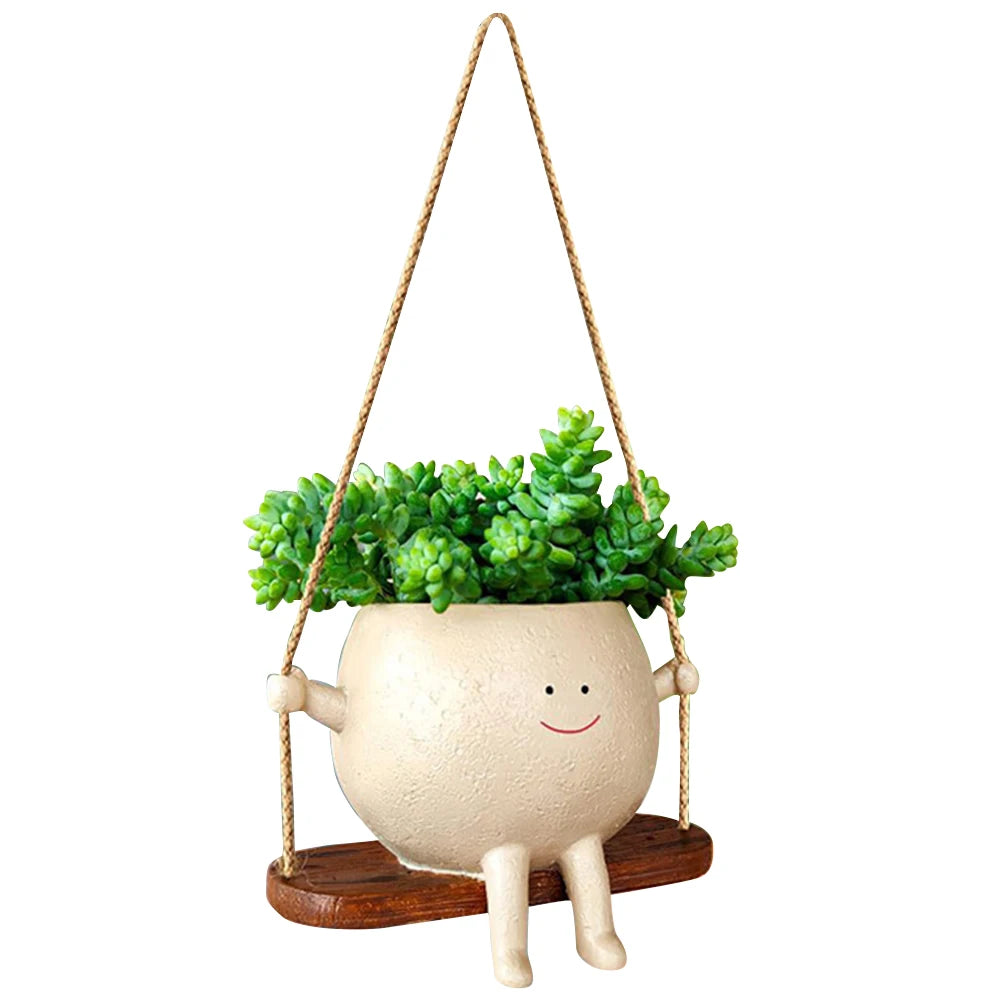 Smiling face planter with succulents hanging on a rope swing, white background